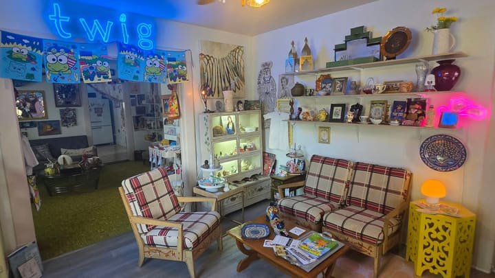 Inside Twig: a blue neon "twig" sign over a cozy lounge with plaid vintage chairs, curio shelves and a yellow side table