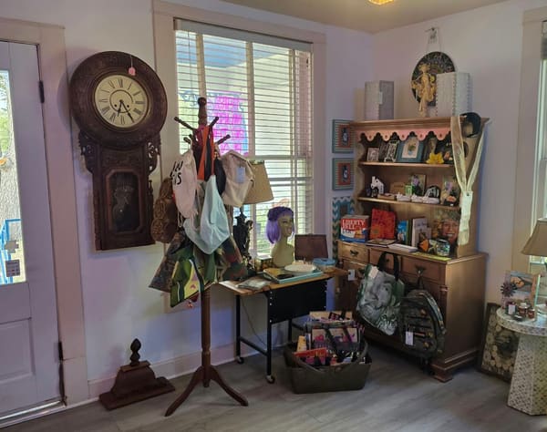 A sunny corner with an antique wall clock, a coat rack hung with bags and a hutch of small treasures