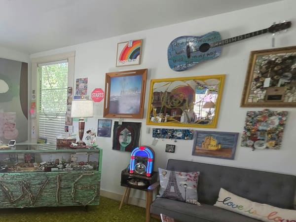 A gallery wall of local artwork, including a hand-painted guitar, framed paintings and a mosaic mirror, above a little jukebox