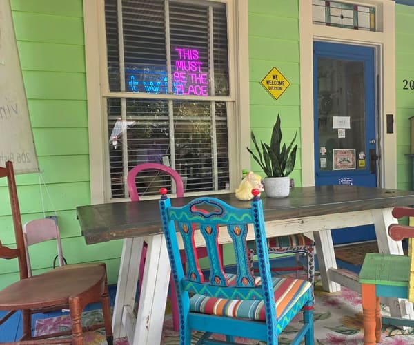 Twig's front porch: hand-painted chairs around a farmhouse table, a pink neon sign in the window and the blue front door at number 206